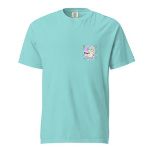 May include: A light turquoise short-sleeved t-shirt featuring a small graphic on the left chest. The graphic depicts a pastel-coloured puppy with the word Paws written in a stylised font, surrounded by small lightning bolt and star icons.