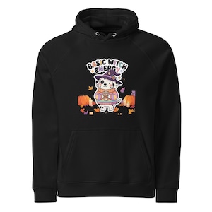 Könnte beinhalten: Ein schwarzer Kapuzenpullover mit einer Grafik eines Dalmatiners, der einen violetten Hexenhut und einen gestreiften Pullover trägt und einen Kaffeebecher hält. Der Text BASIC WITCH ENERGY steht darüber, umgeben von Kürbissen und Kerzen.