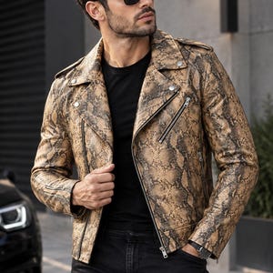 Pode incluir: Um casaco de motociclista em pele com padrão de pele de cobra em tons de bege e preto, com lapela larga, fechos de metal prateado na frente e nos punhos, presilhas nos ombros, usado sobre uma t-shirt preta e calças de ganga pretas.