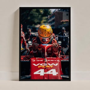 May include: A framed photograph of a race car driver wearing a yellow helmet with the number 44, seated in a red Formula 1 car. The car features the text VGW PLAY and the number 44 on the front nose cone, with an HP logo on the halo structure.