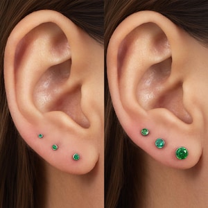 May include: A set of three round green gemstone stud earrings in metal settings, displayed in two different size variations on an earlobe. The studs feature a vibrant green circular stone secured within a polished metal bezel setting.