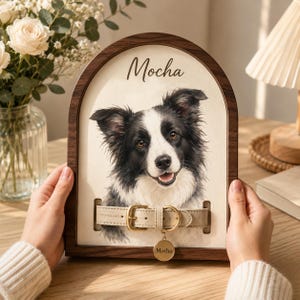 May include: An arched wooden frame containing a portrait of a black and white dog with the name Mocha printed above. A beige leather collar with a gold buckle and a round gold tag engraved with the name Mocha is attached to the portrait surface.