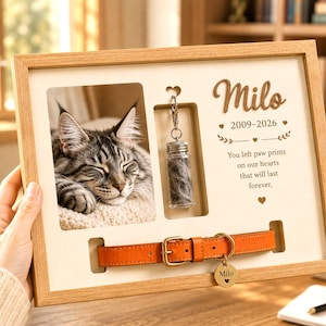 May include: A light wood memorial shadow box frame featuring a photo of a tabby cat, a small glass vial containing fur, and an orange leather collar with a metal tag engraved with the name Milo and the dates 2009-2026, plus a memorial quote.