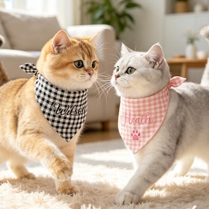 May include: Two cats wearing triangular pet bandanas. The golden cat wears a black and white gingham bandana embroidered with the name Wilson. The silver cat wears a pink and white gingham bandana embroidered with the name Heath and a paw print.