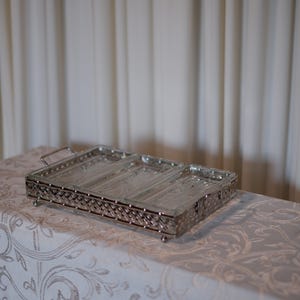 May include: A rectangular glass serving tray featuring three divided sections with a textured, pressed pattern. The tray is encased in a polished silver-tone metal frame with a woven lattice design, small ball feet, and two side handles.