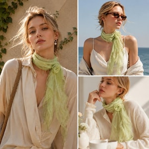 May include: A light green sheer scarf featuring a ruffled texture and a decorative fabric flower accent. The scarf is worn wrapped around the neck, showcasing its lightweight, semi-transparent material and soft, flowing drape against various tops.