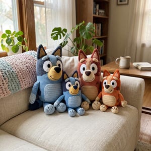 May include: Four crocheted plush toys representing cartoon dogs. Two are blue with darker blue patches and two are reddish-brown with darker brown patches. Each has large white eyes, a tan muzzle, a black nose, and a stitched smile on a sofa.