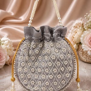 May include: A round grey drawstring handbag featuring a diamond-stitched pattern embellished with white pearl clusters. The bag includes a pearl-beaded handle and two gold-toned braided drawstrings with dangling pearl-accented tassels at the ends.