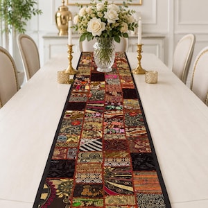 May include: A rectangular table runner featuring a patchwork design composed of various fabric squares. Each square displays distinct patterns, including floral motifs, geometric shapes, and metallic embroidery in shades of gold, red, and black.