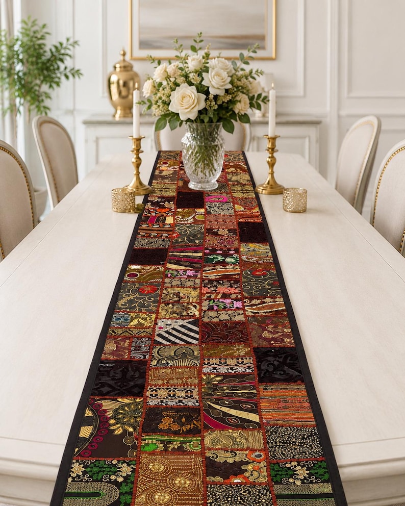 May include: A rectangular table runner featuring a patchwork design composed of various fabric squares. Each square displays distinct patterns, including floral motifs, geometric shapes, and metallic embroidery in shades of gold, red, and black.