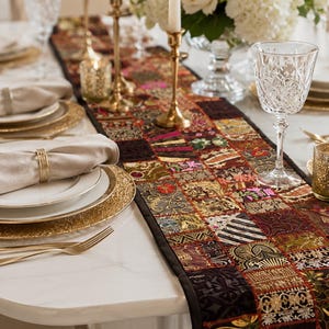 May include: A rectangular table runner featuring a patchwork design of various dark-toned fabric squares with intricate gold, red, and green embroidery, metallic thread accents, and floral patterns, finished with a solid black fabric border.