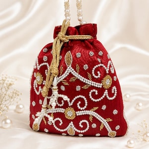 May include: A deep red velvet drawstring pouch featuring intricate white pearl beadwork and gold thread embroidery in a swirling floral pattern. The bag includes a gold braided cord closure and a handle made of white pearl beads for carrying.