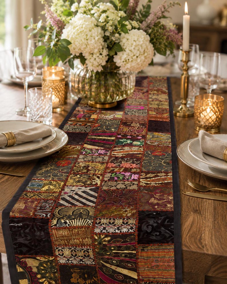 May include: A rectangular table runner featuring a patchwork design of various fabric squares in shades of black, gold, red, and green. The runner displays intricate embroidery, metallic threads, and diverse patterns, finished with a solid black border.