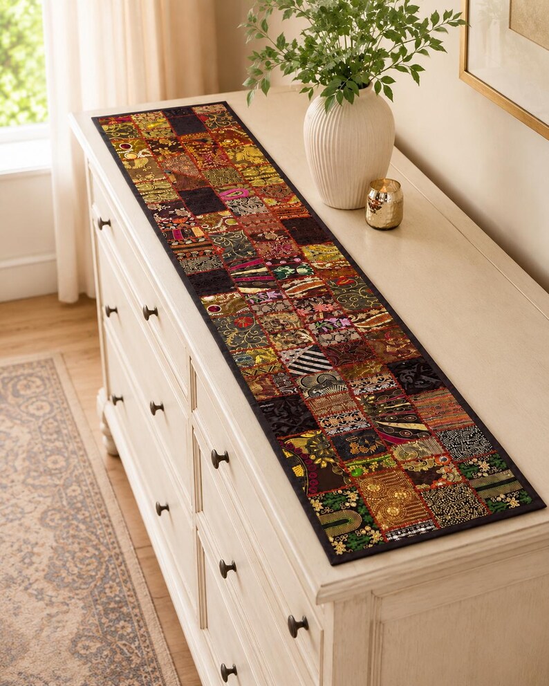 May include: A long, rectangular table runner featuring a patchwork design composed of numerous small, square fabric panels. Each panel displays a unique combination of dark, rich colours, intricate metallic embroidery, sequins, and varied textures.