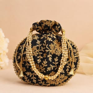 May include: A black drawstring pouch bag featuring intricate gold floral embroidery throughout. The bag includes a handle made of multiple strands of small white faux pearls, accented with gold-toned metal beads and conical end caps at the base.
