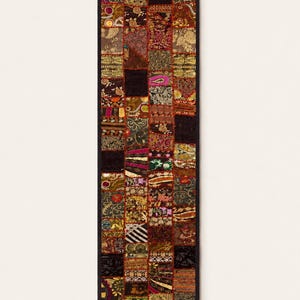 May include: A rectangular table runner featuring a patchwork design composed of numerous small, square fabric panels. The panels display a variety of intricate patterns, including floral, paisley, and geometric motifs in shades of gold, red, black, and green, all bordered by a solid black trim.