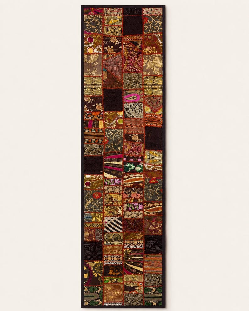 May include: A rectangular table runner featuring a patchwork design composed of numerous small, square fabric panels. The panels display a variety of intricate patterns, including floral, paisley, and geometric motifs in shades of gold, red, black, and green, all bordered by a solid black trim.