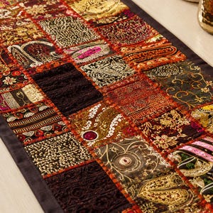 May include: A rectangular table runner featuring a patchwork design of various fabric squares in shades of red, gold, black, and orange. The squares are decorated with intricate metallic embroidery, sequins, beads, and textured lace patterns.