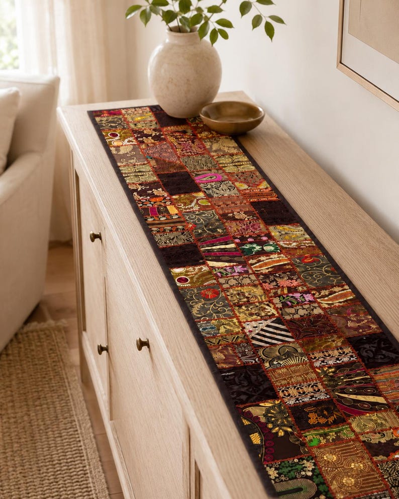 May include: A long, rectangular table runner featuring a patchwork design composed of numerous small, square fabric panels. Each panel displays distinct, intricate embroidery, metallic thread accents, and varied patterns in dark, rich, and vibrant colours.