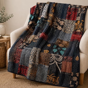 May include: A patchwork quilt featuring a variety of square fabric panels in dark blue, red, gold, and black tones. The quilt displays intricate floral and geometric patterns with visible white running stitch details throughout the entire surface.