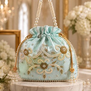May include: A light blue drawstring handbag featuring intricate embroidery with white pearls, gold metallic thread, and clear beads. The bag has a single top handle made of white pearls and gold-toned cord drawstrings with beaded tassel ends.