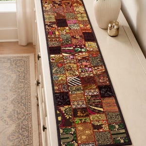 May include: A rectangular table runner featuring a patchwork design of various fabric squares. Each square displays intricate embroidery, metallic thread accents, sequins, and diverse patterns in shades of gold, red, green, and black.