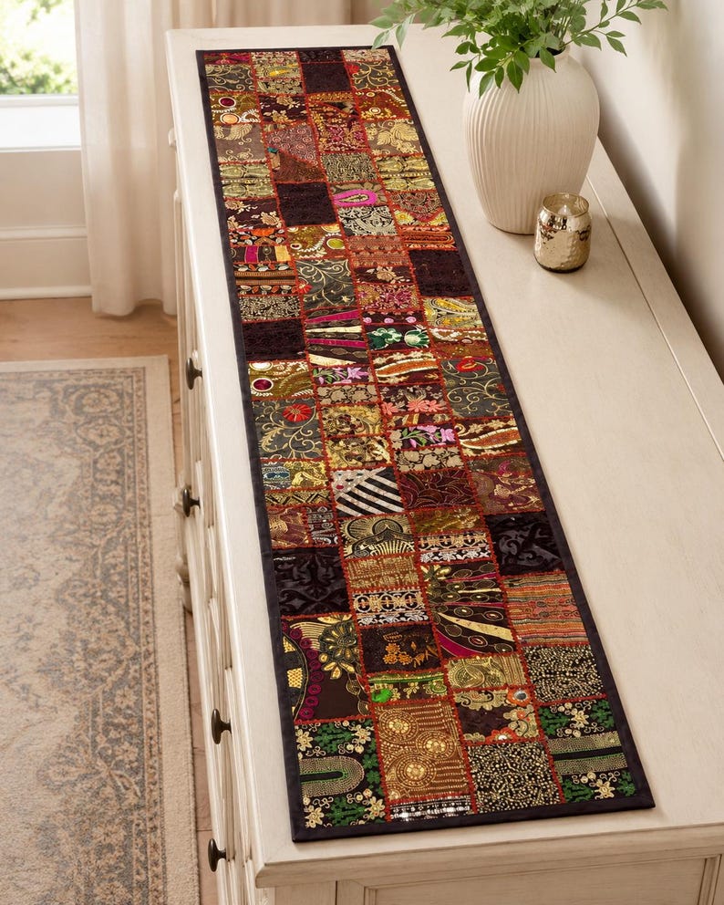 May include: A rectangular table runner featuring a patchwork design of various fabric squares. Each square displays intricate embroidery, metallic thread accents, sequins, and diverse patterns in shades of gold, red, green, and black.