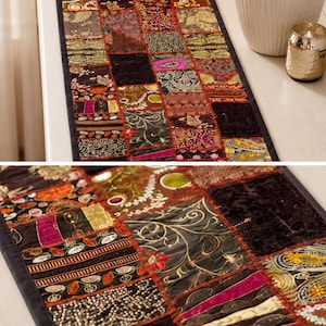 May include: A rectangular table runner featuring a patchwork design of various dark-toned fabric squares. The runner includes intricate gold embroidery, metallic thread accents, sequins, and floral patterns in shades of burgundy, black, and gold.