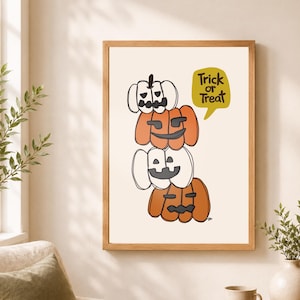 May include: A framed wall art print featuring a vertical stack of four stylized pumpkins in alternating white and orange colors with carved faces. A yellow speech bubble to the right contains the black text Trick or Treat.