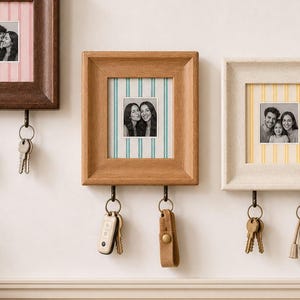 May include: Three rectangular wall-mounted photo frames in dark brown, medium brown, and cream wood finishes. Each frame features a vertical striped mat and two metal hooks at the bottom for hanging keys. Black and white photos are displayed inside.