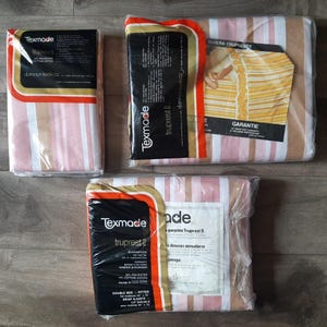 May include: Three packages of Texmade Truprest II bed sheets in plastic wrap. The sheets feature vertical stripes in shades of pink, white, and tan. Each package includes black and orange labels with product details and the Dominion Textile brand name.