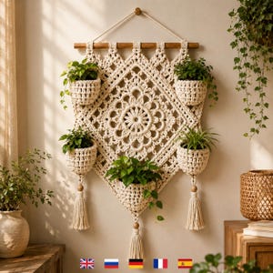 Puede incluir: Un tapiz de macramé color crema con un patrón central de diamante y cinco bolsillos integrados que contienen plantas verdes. La pieza cuelga de un soporte de madera con una cuerda e incluye borlas decorativas en la parte inferior.