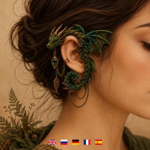 Könnte beinhalten: Ein grüner Drachen-Ohrring mit einer häkelartigen Textur, goldenen Metallakzenten und einer hängenden Goldkette mit einem grünen tropfenförmigen Edelstein sowie einem Blattanhänger. Der Drache umschließt das Ohr mit Flügeln und einem Schwanz.