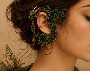 May include: A green dragon ear cuff featuring intricate crochet-like texture, metallic gold accents, and a dangling gold chain with a green teardrop gemstone and a leaf charm. The dragon wraps around the ear with detailed wings and a curled tail.