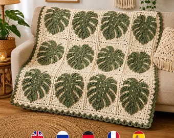 May include: A rectangular crochet blanket featuring a grid of twelve dark green monstera leaf motifs set against a cream-colored background. The blanket is finished with a scalloped border in the same dark green yarn as the leaf designs.
