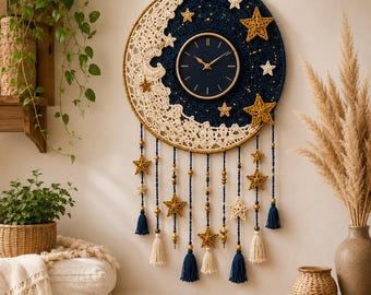 May include: A circular wall clock featuring a dark blue center with gold hands, surrounded by a crocheted crescent moon in cream and a dark blue night sky background. The piece is adorned with gold and cream crocheted stars and hanging beaded tassels.
