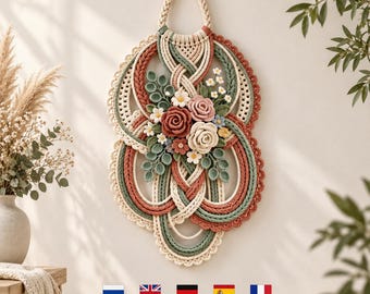May include: A wall hanging featuring intricate macrame cord loops in cream, sage green, and terracotta. The center is adorned with a cluster of fabric flowers in shades of pink, cream, and white, accompanied by small green fabric leaves and stems.