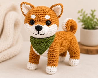 May include: A crochet Shiba Inu dog toy featuring golden-brown and white yarn, black plastic eyes, and a black embroidered nose. The dog wears a textured green triangular bandana around its neck and has white paws and a curled tail.