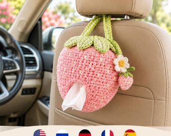 May include: A pink crocheted strawberry-shaped tissue holder with a green stem handle and a small white flower and strawberry charm attached to the side. The holder features a bottom opening for dispensing tissues and hangs from a car headrest.