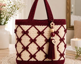 May include: A cream-colored crochet tote bag featuring a dark maroon lattice pattern with small bows at each intersection. The bag has two matching maroon handles and a decorative tassel charm with wooden beads and a heart-shaped wooden pendant.