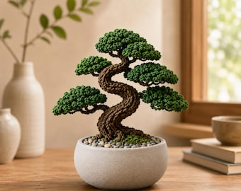 May include: A crocheted bonsai tree with a textured brown trunk and vibrant green foliage, potted in a round, light gray ceramic container filled with small, smooth, multi-colored pebbles at the base, creating a detailed fiber art sculpture.