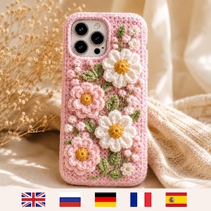 May include: A pink crocheted phone case featuring three-dimensional floral embellishments. The design includes white daisies with yellow centers, pink flowers with yellow centers, and small green leaves and stems stitched onto the textured surface.