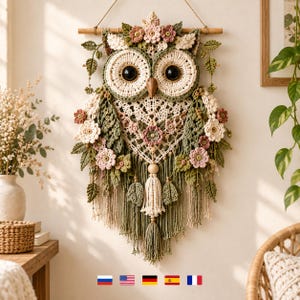 May include: A wall hanging featuring a crocheted owl with large dark eyes, a wooden beak, and intricate cream and sage green yarn details. The owl is adorned with crocheted flowers in shades of pink and cream, hanging from a wooden dowel with tassels.