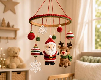 Puede incluir: Un móvil colgante con adornos navideños de ganchillo que incluyen una figura de Papá Noel, un reno con bufanda verde, copos de nieve blancos y esferas a rayas rojas, verdes y blancas suspendidas de un marco circular de madera con hilos rojos.