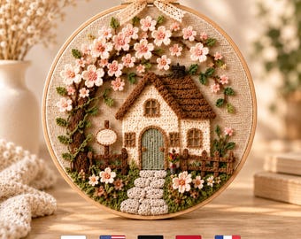 May include: A circular embroidery hoop featuring a crocheted cottage scene with a brown roof, cream walls, and a green door. A tree with pink blossoms arches over the house, with a stone path, a wooden fence, and a cream lace bow at the top.