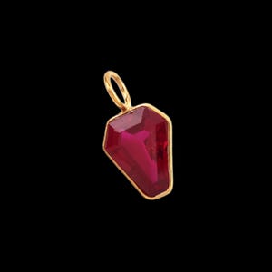 Peut inclure: Un pendentif composé d'une pierre précieuse rouge foncé à facettes en forme de cercueil, enchâssée dans une fine monture en métal doré. La pièce comprend une petite bélière circulaire dorée sur le dessus pour l'attacher à une chaîne ou un cordon.