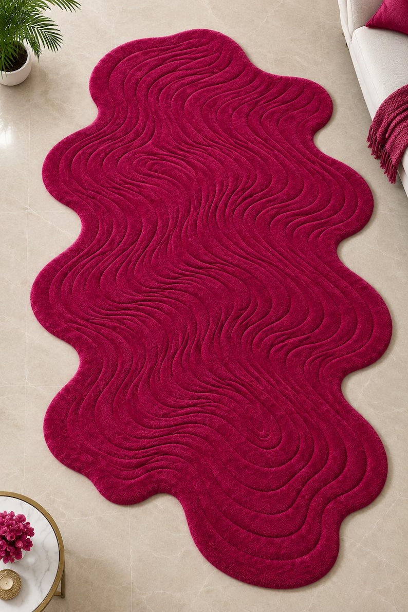 May include: A deep magenta area rug with an irregular, organic, wavy shape. The surface features a textured, rippled pattern of concentric, flowing lines that mimic the appearance of liquid movement across the entire length of the rug.