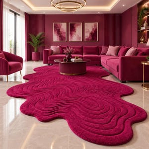 May include: A large, irregular, magenta-colored area rug with a textured, wavy, concentric pattern. The rug features a soft, plush surface and is shaped like a fluid, organic puddle, covering a significant portion of the light-colored floor.