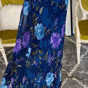 May include: A long, navy blue skirt with a floral print featuring purple, blue, and green flowers. The skirt is made of a sheer fabric and has a flowy silhouette.