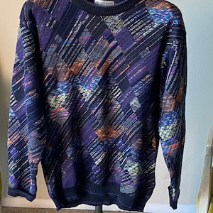 May include: A purple, black, and orange patterned sweater with a crew neck. The sweater has a label that reads "Benetton".